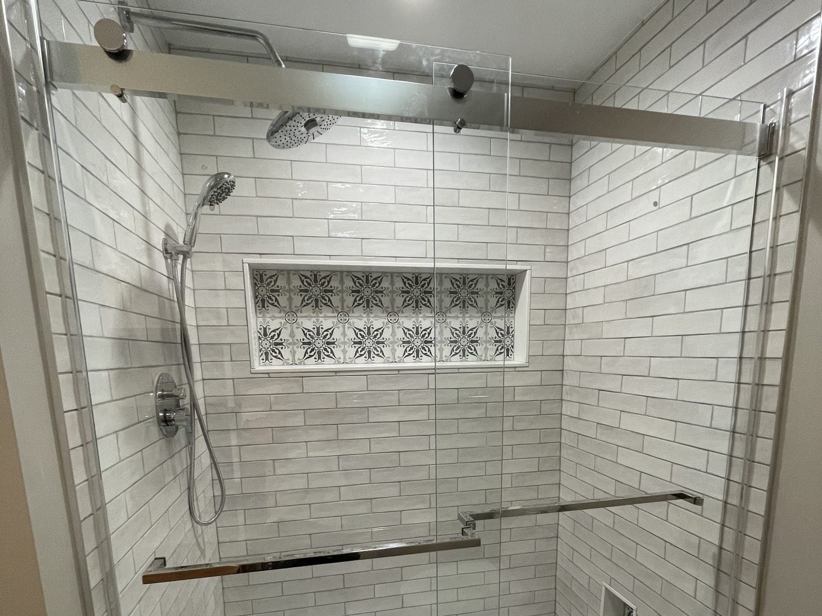 Walk-in shower with white subway tile, a patterned tile niche, a rain shower head and a sliding glass door.