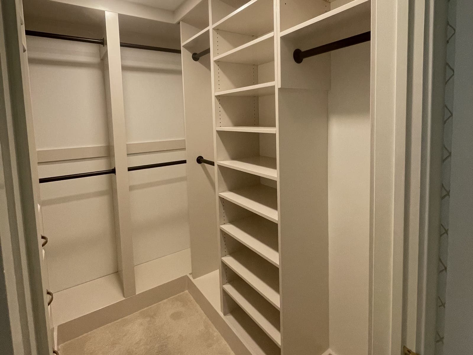 A walk-in closet built-in seen from the doorway: white shelving towers with adjustable shelves, double and single hanging rods in dark bronze, and carpet.