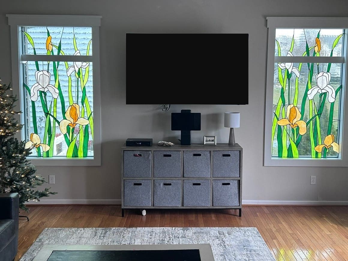 Living room with two tall windows in white trim, a decorative film on the glass, a wall-mounted TV between them over a cube shelf, and a wood floor.